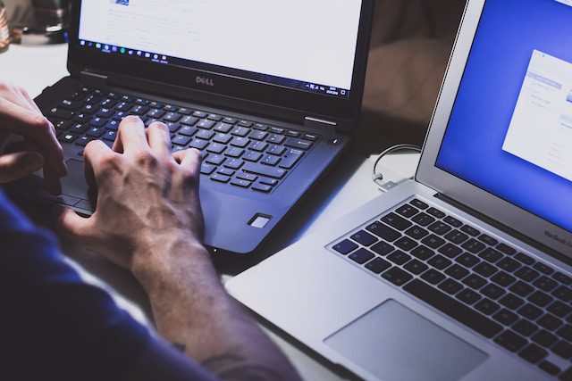 person in front of two open laptops, with fingertips touching the touchpad on a black laptop's keyboard